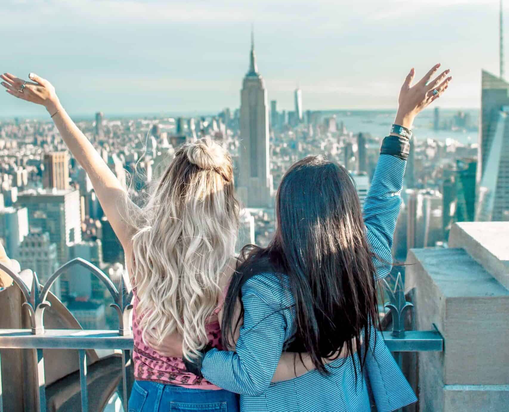 Due giovani donne che guardano dei grattacieli, si abbracciano e gioiscono