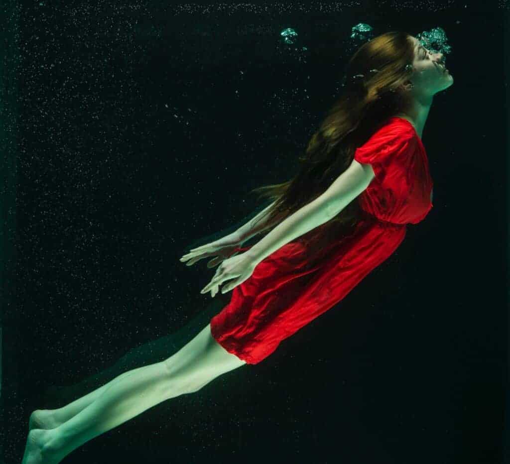 Frau mit rotem Kleid schwimmt unter Wasser