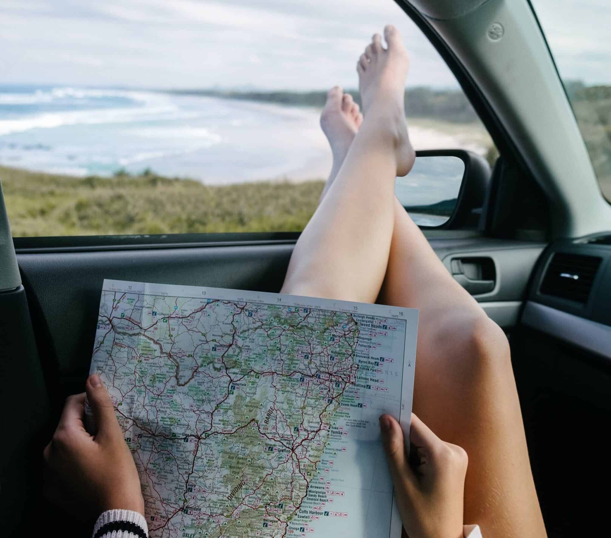 Legs hang out of the car window with a map on their laps