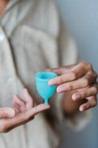 Eine Person hält eine Menstruationstasse zwischen zwei Fingern