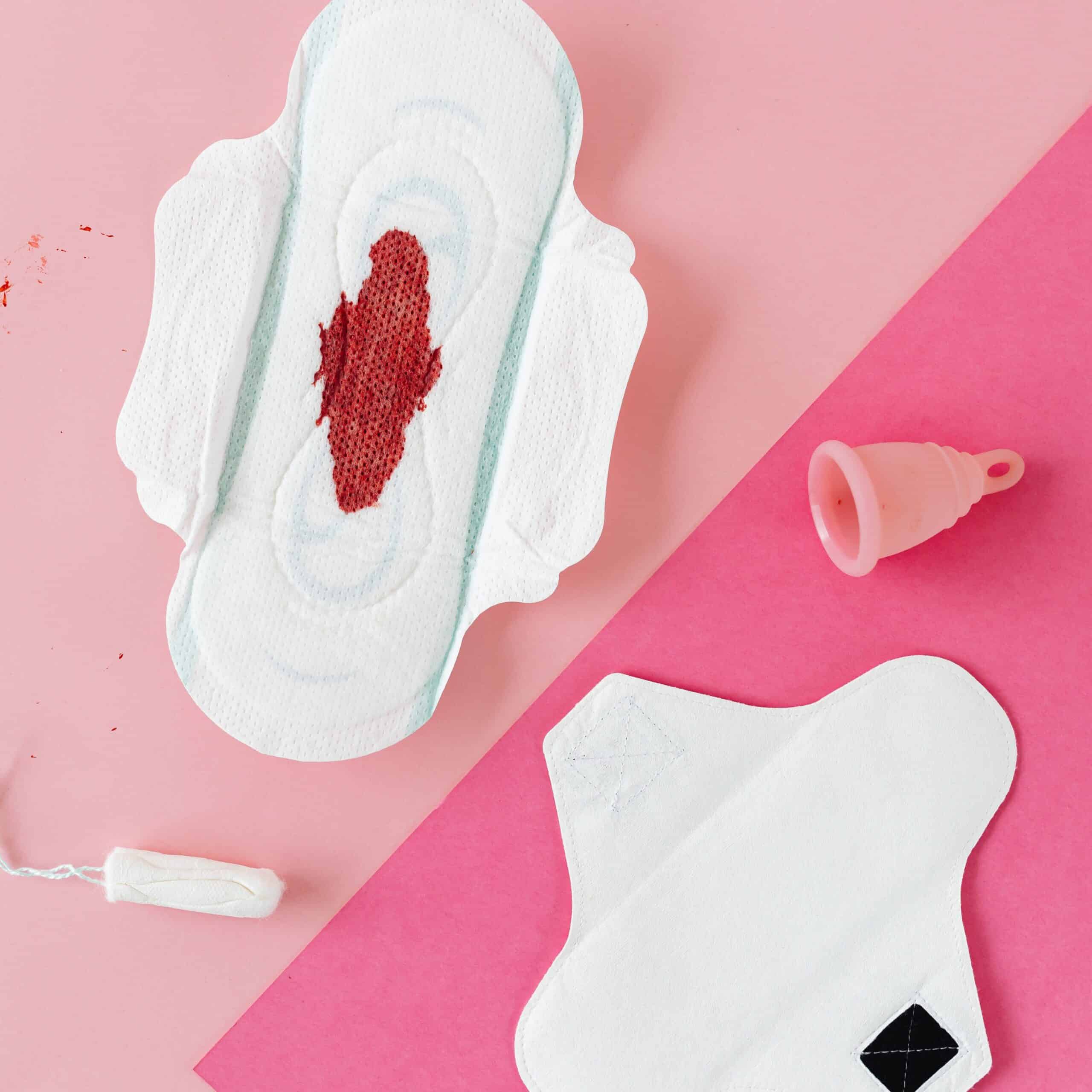 Menstruationstasse, Binde, Tampon und Einlage liegen gemeinsam auf einem Untergrund